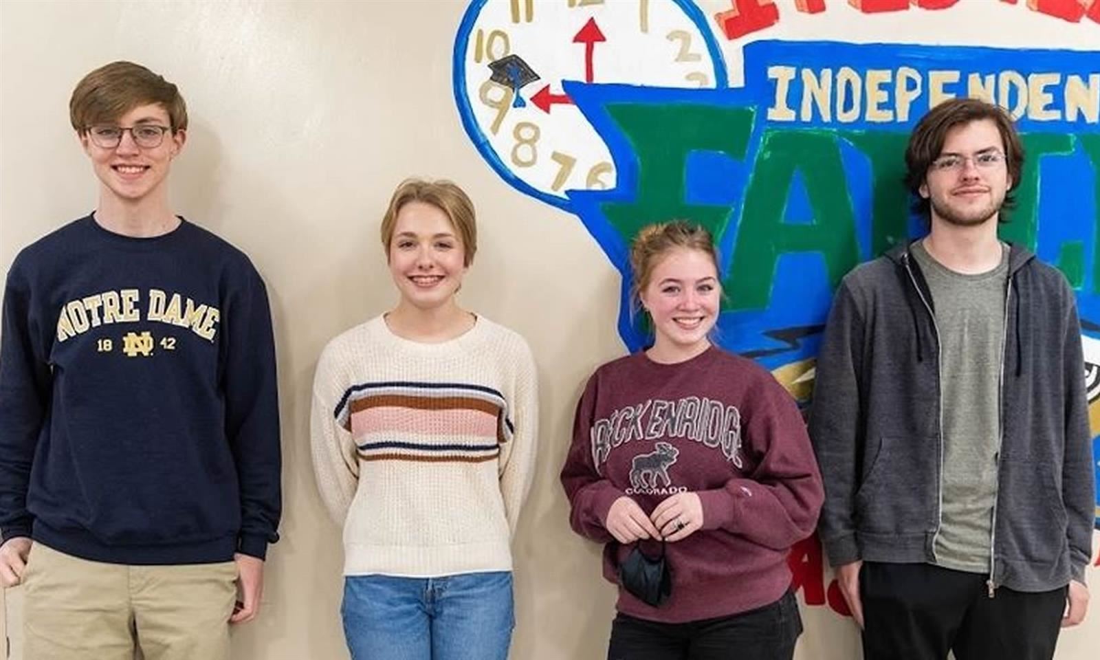 Four students stand against a wall 